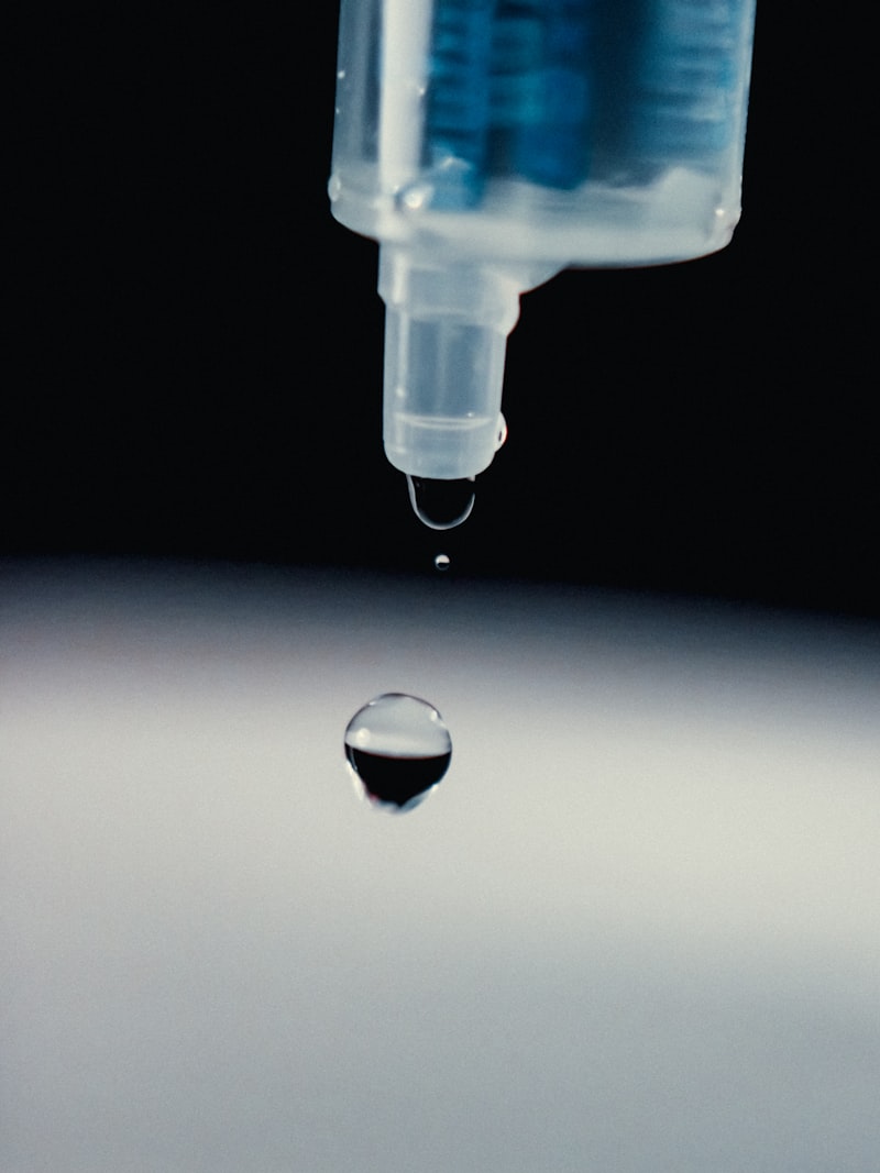 Syringe dispensing clear adhesive droplet against dark background for Uni-Weld™ UV doming and glob top encapsulation